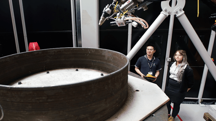 Two people stand by manufacturing equipment